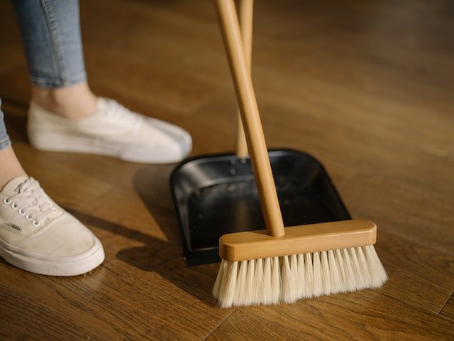 A Landlord In White Sneakers Sweeps The Hardwood Floor Of Their Rental Property With A Bamboo Broom