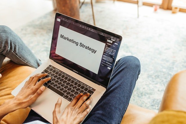 A-Person-Typing-On-A-Laptop-With-Marketing-Strategy-Written-Across-The-Screen