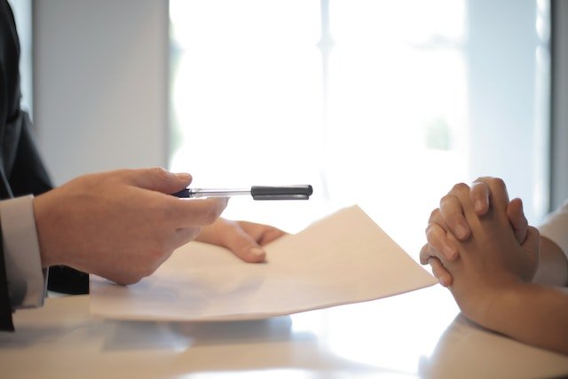 A-Person-Handing-Documents-And-A-Pen-To-Another-Person