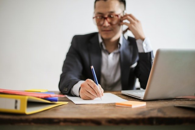 Person Talking On The Phone While Taking Notes At Their Desk
