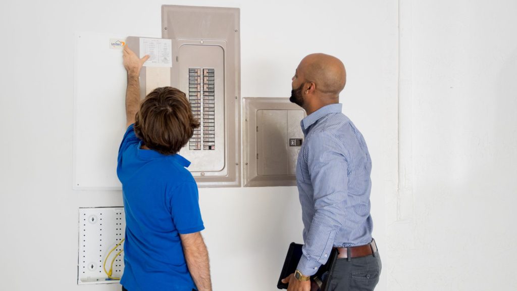 A Property Manager Looking At A Switchboard With A Maintenance Technician.